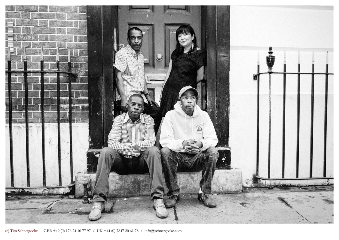 Black and white picture of three men and one lady, two of whom are sitting on a step, the other two who are standing behind them