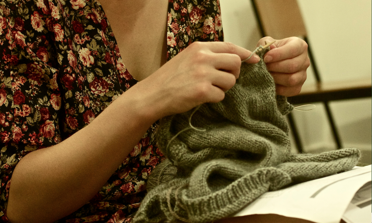 A lady wearing a floral top knitting a green jumper