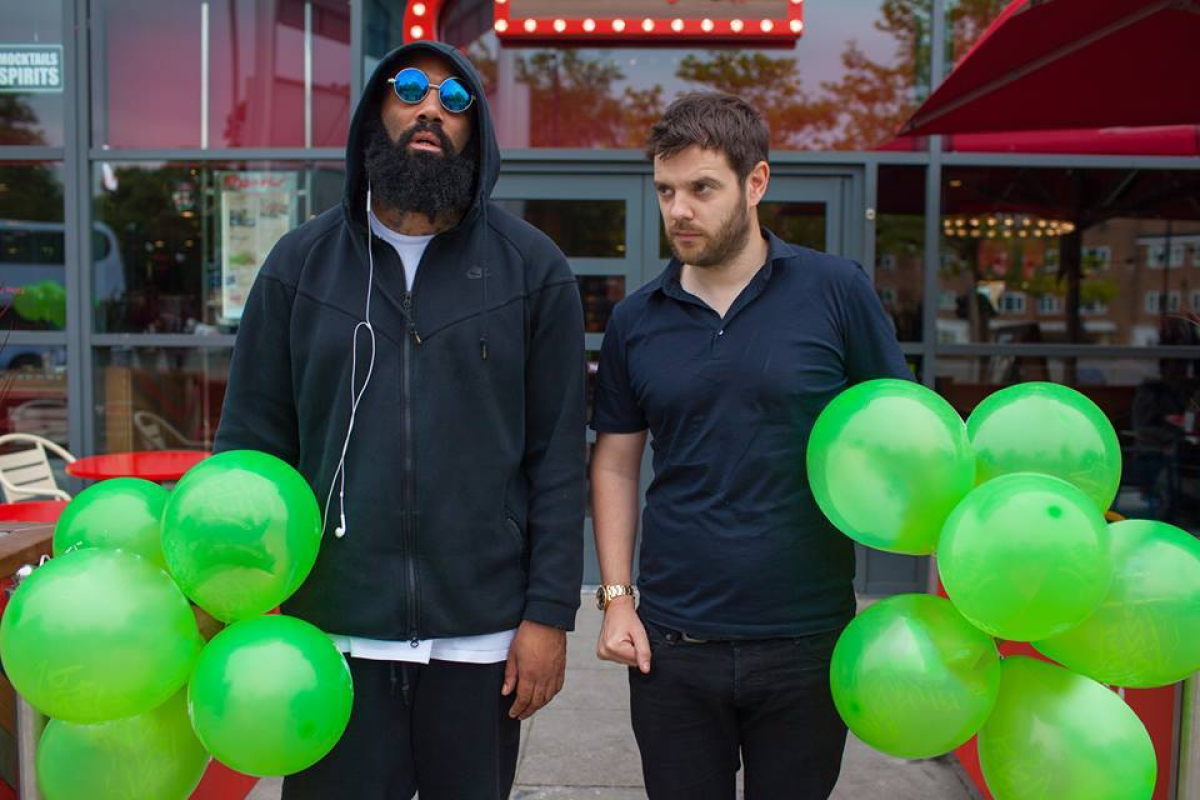 Two men wearing black holding green balloons.