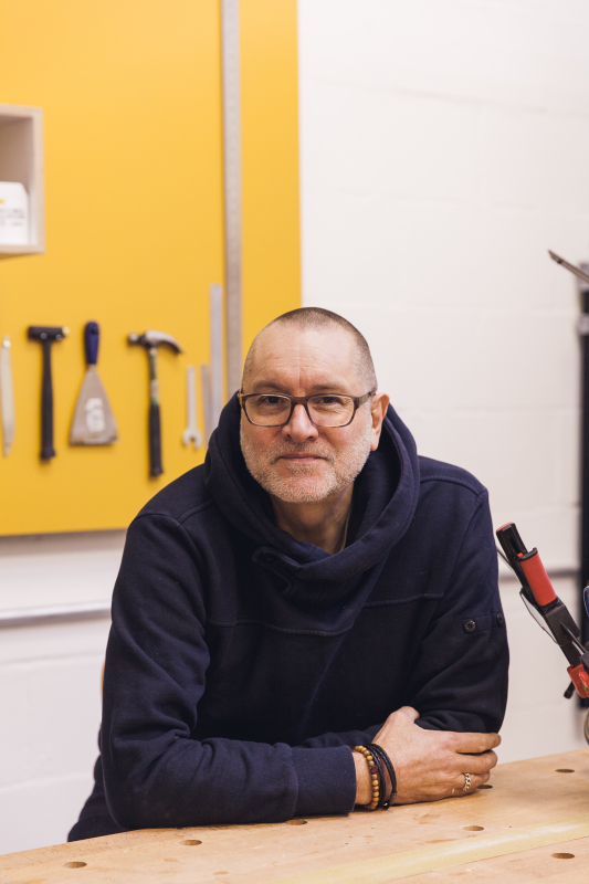 A man in his workspace with tools in the background.