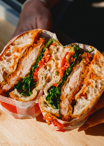 Close-up of Bread Meats Sauce’s crispy chicken sandwich with fresh greens, roasted peppers and spicy mayo in artisan ciabatta, served at Netil Market