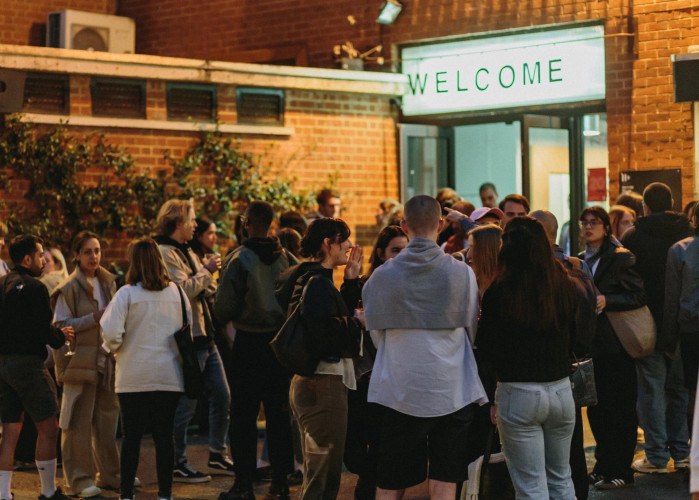Evening community gathering outside Hackney Downs Studios with creatives mingling under illuminated Welcome sign