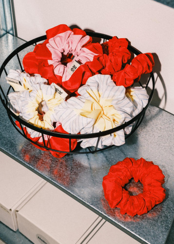 Close-up of Hobul Studios scrunchies in red, pink and pastel tones arranged in a wire basket on a metal shelf, displayed at Netil Market