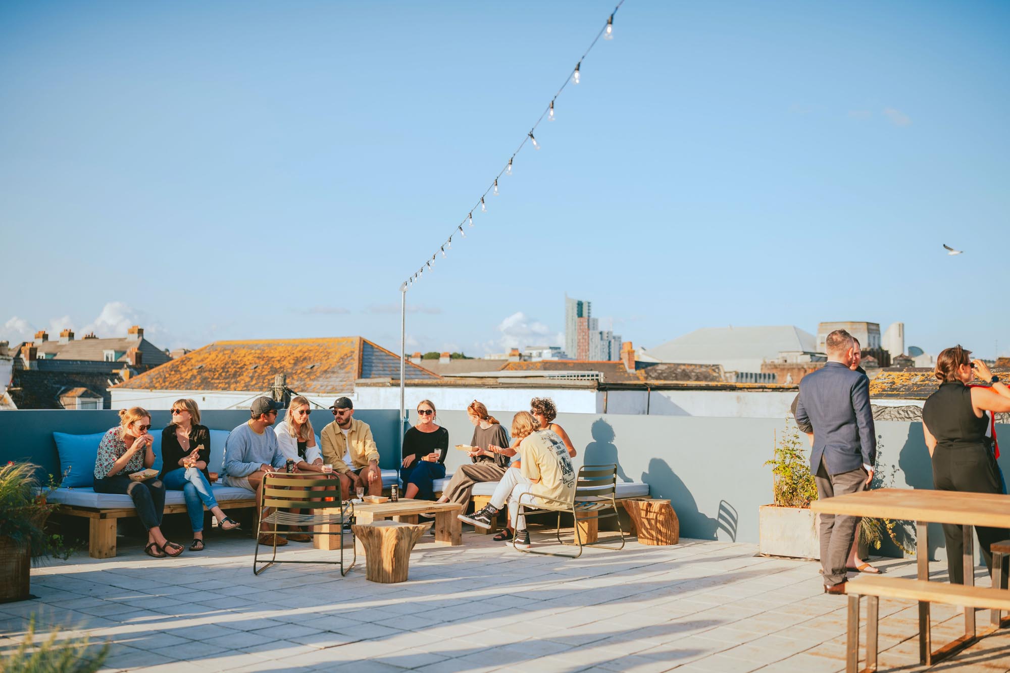 Creative residents and guests socialising on the rooftop terrace at Light Studios Plymouth, with skyline views and outdoor seating in warm evening light