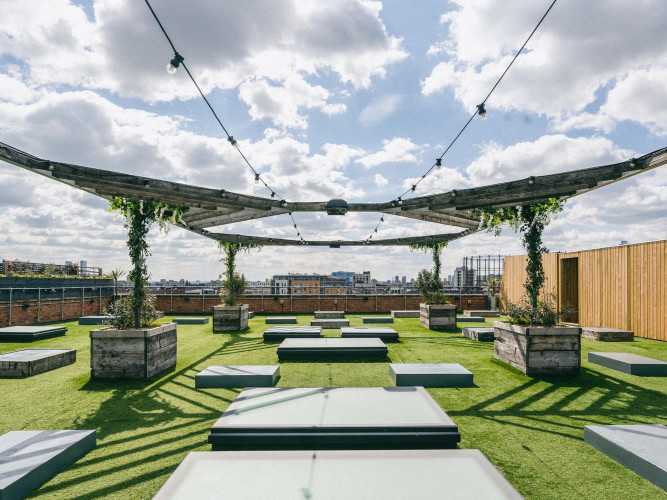 Open-air rooftop garden at Netil Corner London with turf seating, pergolas and panoramic skyline views – a versatile outdoor event space